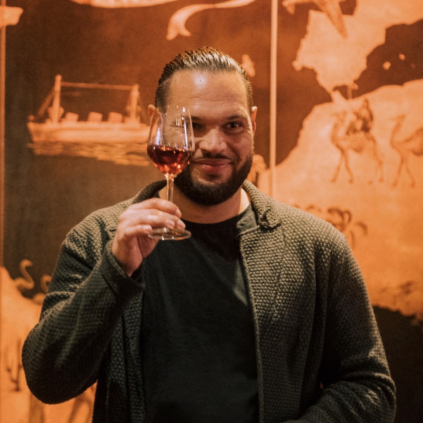 Andy Gas, Gründer von La Vida Loca, hebt ein Glas Wein vor einer Wand mit alter Weltkarte