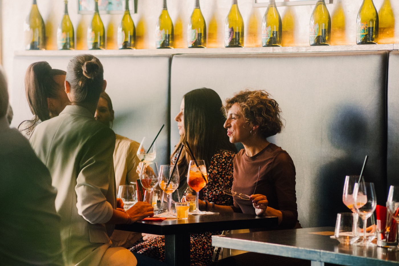 Gäste mit Drinks an einem Tisch vor einem Weinregal