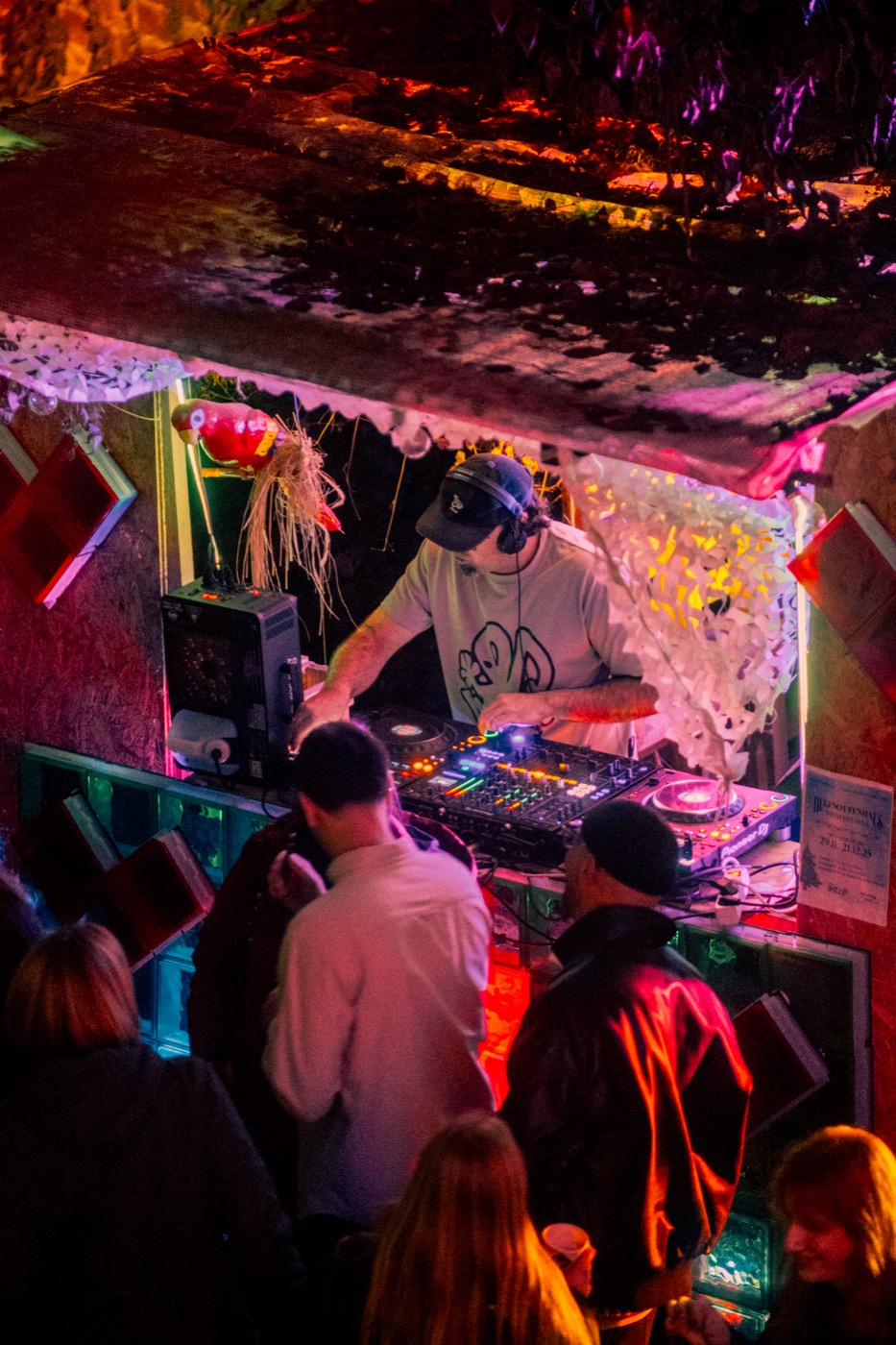 DJ an der Booth mit buntem Licht vor tanzenden Gästen