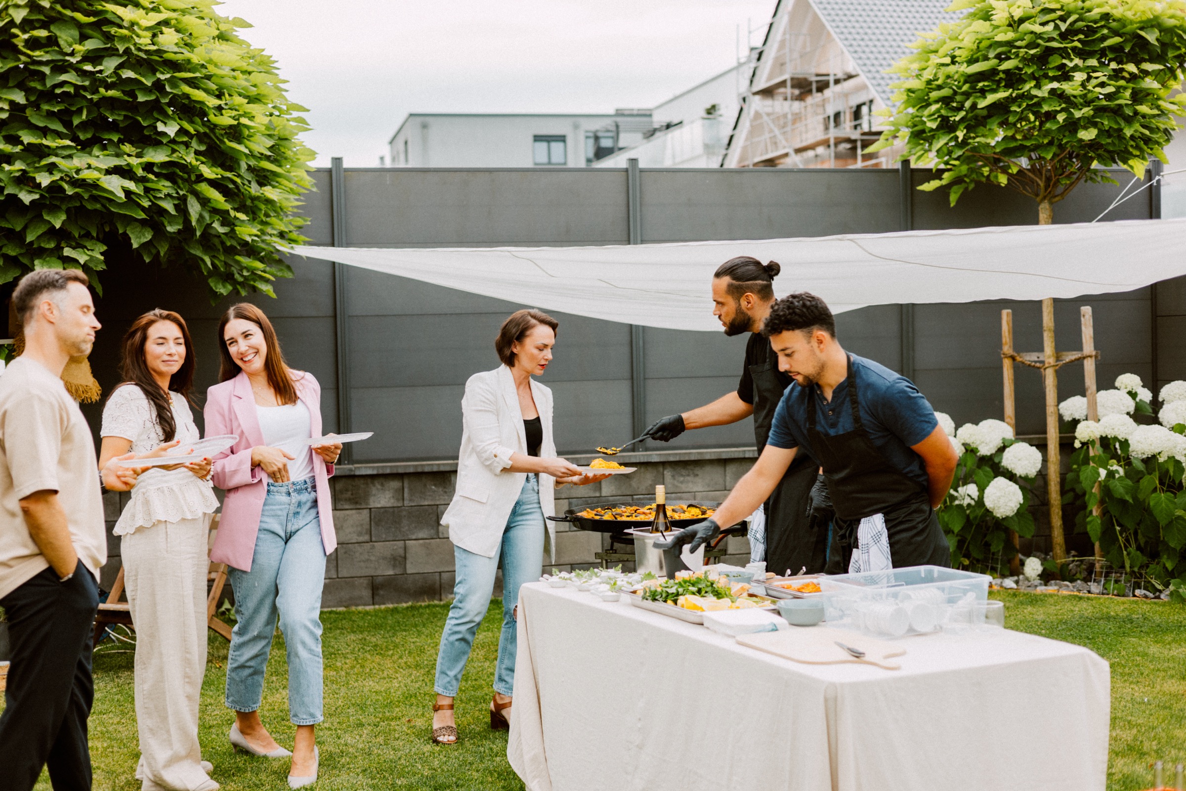 Live-Catering im Garten: Koch serviert frisch zubereitete Paella an Gäste bei einem privaten Sommer-Event